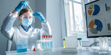 Modern bir laboratuvarda, koruyucu giysiler içindeki bir bilim adamı, yüksek teknolojili bir bilgisayardaki verileri analiz ederken, bilimsel araştırmalarda yenilik ve ilerleme gösterirken test tüpleri üzerinde deneyler yapar.