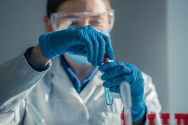 Koruyucu giysiler içindeki yetenekli bir laboratuvar teknisyeni temiz bir test tüpüne bir reaktör ekliyor. Başarılı bilimsel deneyler için gerekli olan hassasiyeti gösteriyor.