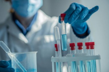 Laboratuvar önlüğü ve eldivenleriyle çalışkan bir bilim adamı, bilimsel araştırma ve deneylerde hayati önem taşıyan detayı gösteren renkli test tüplerini dikkatle yönetir.