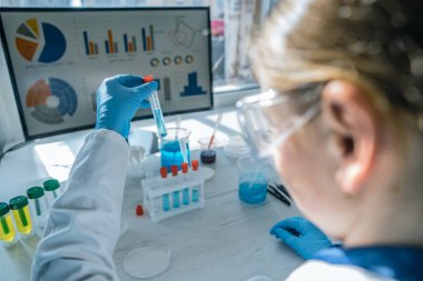 Laboratuvar önlüğü giymiş kendini adamış bir bilim adamı renkli test tüpleriyle detaylı bir deney yapıyor. Kimyasal analizlerin ve ileri araştırma tekniklerinin canlı ve karmaşık alanını gözler önüne seriyor.