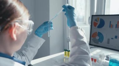 Modern bir laboratuvarda, yetenekli bir bilimadamı deneyler için hassas bir pipet kullanırken, organize ekipmanlarla çevrili büyük bir ekrandaki verileri analiz ederek, araştırmaya güçlü bir bağlılığı yansıtır.