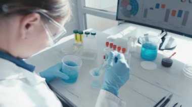 Bir laboratuvarda, kendini adamış bir bilim adamı kimyasal çözümleri karıştırır ve verileri bir ekranda analiz eder, araştırma ve bilimsel keşif ve keşif yoğunluğundaki gelişmeleri gösterir.