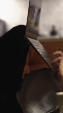 Bir insan rahat bir kanepeye uzanır, yumuşak ışıklı bir odada dizüstü bilgisayarla çalışır, yanında dumanı tüten bir fincan kahveyle, esinlenerek ve yaratıcılıkla dolu sakin bir çalışma ortamını somutlaştırır.