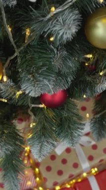Güzel dekore edilmiş bir Noel ağacında canlı kırmızı ve altın süsler, yanıp sönen ışıklar ve altında renkli hediyeler sergilenir, şenlik kutlamalarının neşesi ve ruhunu somutlaştırır.
