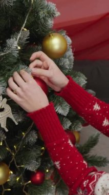 Bir insan, güzel süslenmiş bir Noel ağacını altın ve kırmızı süslemelerle süslüyor. Bayramların neşeli ruhunu neşe ve sevgi dolu sıcak bir atmosferde yakalıyor.