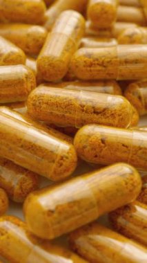 Turuncu kapsüller ve biberli diyet takviyesi. Beyaz arka planda kapsül koleksiyonu, sağlığın ritmine göre dönüyor. Sağlıklı Yaşamın Yolu: İlaç Endüstrisi