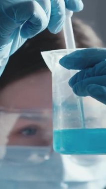 PPE 'deki bir araştırmacı canlı mavi sıvıyla test tüpünü inceliyor, bilimsel araştırmaların özünü yakalıyor ve araştırma ortamlarında güvenlik protokollerinin önemini vurguluyor.
