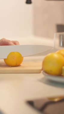 Bir birey, modern bir mutfağın sağlam ahşap kesim tahtasındaki taze, canlı limonları ustalıkla dilimliyor. Renkli meyvelerle çevrili, hepsi de besleyici bir yemeğe hazırlanıyor.