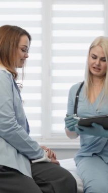 Modern bir tıp kliniğinde kadın bir hastaya sağlık hizmeti veren profesyonel bir danışman. Sağlık hizmetlerine kapsamlı ve teknolojik bir yaklaşımın göstergesi olan dijital tablet hakkındaki bilgileri gözden geçirirler.