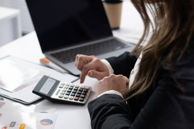 Takım elbiseli bir iş adamı, bir dizüstü bilgisayar ve belgelerle çevrili bir hesap makinesine odaklanır. Bu da dikkatli bir finansal analiz ve stratejik karar verme anını yansıtır.