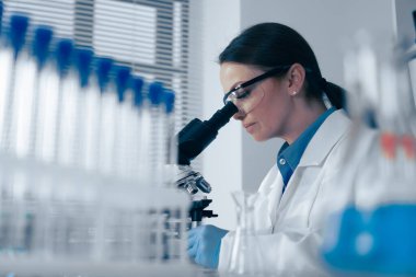 Bir bilim adamı laboratuvarda mikroskop altında bir örnek üzerinde çalışıyor. Bilim, teknoloji ve yenilikçi keşifler için gerekli olan test tüpleri ve ekipmanlarla hayati araştırmalar yapıyor.
