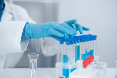 Beyaz önlüklü ve mavi eldivenli kendini adamış bir bilim adamı bilimsel araştırma ve deneylerde hassasiyet ve özen gösteren modern bir laboratuvarda test tüplerini titizlikle tutuyor.
