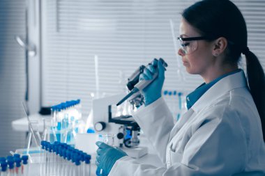 Laboratuvarda, bir bilim adamı deney tüpleri ve ekipmanlarla çevrili örnekleri analiz etmek için bir pipet kullanır. Doğa ve sağlık anlayışımızı geliştirmek için çığır açan keşifleri amaçlar.