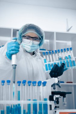 Temiz bir laboratuvarda, koruyucu ekipman kullanan kendini adamış bir bilim adamı deney sırasında doğruluğu ve güvenliği sağlamak için deney tüpleri arasında belirli miktarda sıvı transferi için ustalıkla bir pipet kullanır.
