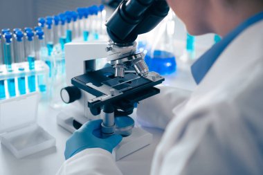 Yoğun bir laboratuvarda, bir araştırmacı test tüpleriyle çevrili örnekleri mikroskop altında inceleyerek modern bilimsel yöntemleri sergiliyor ve bilginin, yeniliğin ve keşfin amansız arayışı