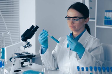 Laboratuvar önlüklü kendini adamış bir bilim adamı ileri mikroskoplar ve çığır açan araştırmalar ve keşifler için gerekli örnekler ile donatılmış bir laboratuarda test tüpünü inceliyor.