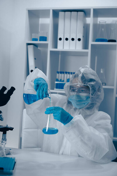 In a clean lab, a dedicated scientist in a lab coat and protective gear is pouring a vibrant blue liquid from a test tube into a beaker, demonstrating precision and expertise in chemistry