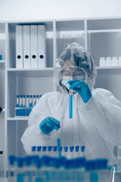 In a lab, a dedicated scientist in PPE carefully combines chemical compounds in a test tube, showcasing precision and a strong commitment to safety protocols during important research activities
