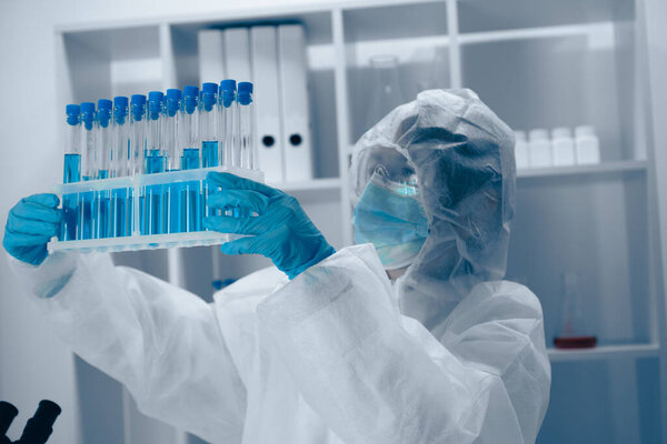 In a hightech lab, a meticulous scientist in protective gear inspects test tubes with vibrant blue liquid, highlighting the importance of safety and precision in complex experiments