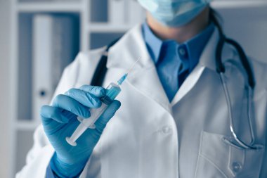 Temiz beyaz önlüklü eğitimli bir sağlık uzmanının elinde şırınga var. Tıbbi araç ve gereçlerle dolu bir klinik ortamında aşıya hazırlanıyor.