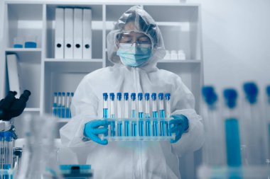 Beyaz önlüklü ve koruyucu teçhizatlı yetenekli bir araştırmacı titizlikle test tüplerini laboratuarda düzenler ve her gün titizlikle bilimsel çalışmalar yapılmasını sağlar.