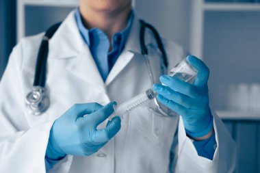 Gıcır gıcır beyaz önlük giyen ve mavi eldiven giyen kendini işine adamış bir tıp uzmanı titizlikle bir şırınga hazırlıyor.