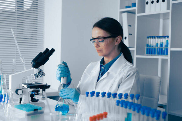 In a wellequipped lab, a scientist in a white coat carefully measures liquid solutions with a pipette, surrounded by essential tools and test tubes for groundbreaking scientific research