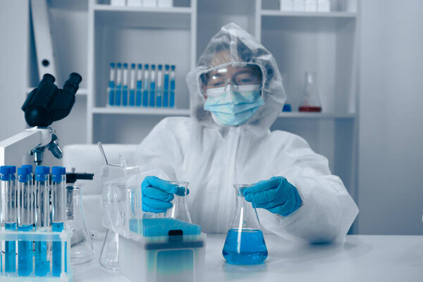 A scientist in protective gear pours a vibrant blue liquid from a flask into a beaker, surrounded by advanced lab equipment in a clean, hightech lab, highlighting their commitment to research