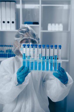 Yüksek teknolojili bir laboratuvarda, koruyucu ekipman araştırmacısı parlak mavi sıvıyla dolu bir test tüpünü inceliyor, titiz bilimsel analizler ve titiz deneylere bağlılığını gösteriyor.