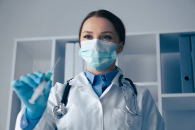 Klinik sağlık ortamında, kürk ve maske giyen şefkatli bir uzman, bir şırınga tutuyor, hastalıklara karşı korunmaya ihtiyacı olan bir hastaya önemli bir aşı uygulamaya hazır.