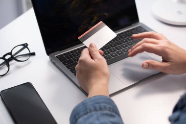 Görüntü, bir kişinin dizüstü bilgisayar kullanırken kredi kartı tutmasını, online alışverişin yükselişini ve gelişmekte olan günlerdeki dijital finansal işlemlerin güvenliğini vurguluyor.