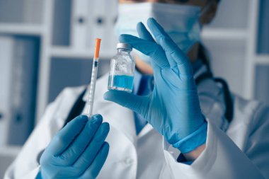 Laboratuvar önlüğü ve eldiveni giymiş bir sağlık uzmanı, şırıngayı ustalıkla tutarken bir aşı şişesini inceliyor ve etkili bir aşıya hazırlanmanın önemini vurguluyor.