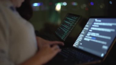 Gecenin sessizliğinde, kendini işine adamış bir yazılım geliştirici yorulmadan birden fazla dizüstü bilgisayarda çalışıyor. Arkaplanı saran çarpıcı şehir siluetine karşı karmaşık kod hatları parlıyor.