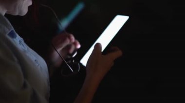 loş bir alanda, bir birey akıllı telefonuna odaklanır, onların ifadesini aydınlatan ve dijital dünyayla ve modern iletişimle olan bağlantılarını vurgulayan parıltı