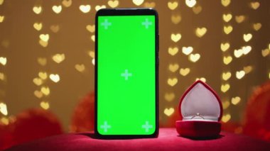 Romantik bir sahne hayal edin. Parlak yeşil ekranlı, kırmızı kadife bir yüzük kutusunun yanında. Hepsi de Sevgililer Günü 'nde yumuşak kalp şeklinde ışıklandırmayla aydınlatılmış.