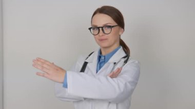 Şık gözlüklü ve beyaz önlüklü kendine güvenen bir kadın doktor, boynunda steteskopla tarafsız bir zemin üzerinde duruyor. Sağlık hizmetlerinde profesyonellik ve şefkat simgeliyor.