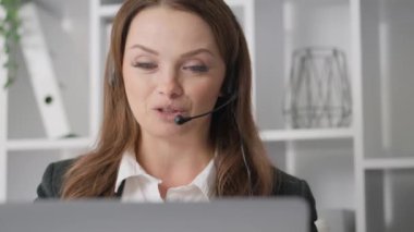 Modern bir ofiste, kulaklıklı neşeli bir iş kadını müşterilerini bilgisayarına alır, istisnai iletişim becerileri, profesyonellik ve üretken etkileşimleri teşvik eder.