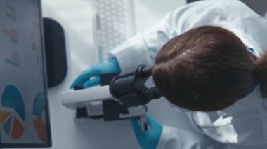 Bir laboratuvarda, odaklanmış bir bilim adamı mikroskop altında örnekleri incelerken, veri görselleştirmeleri bilimsel yeniliğin önemini vurgulayarak karmaşık araştırmalar sergilemektedir.