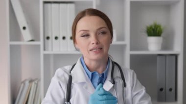 Laboratuvar önlüğü ve steteskopuyla kendini işine adamış bir kadın doktor, düzenli ofisinden izleyicilere seslenerek, hastanın refahı üzerine odaklanmış klinik bir ortamda tedavi ve uzmanlığını sergiliyor.