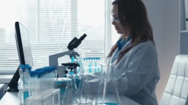 Yoğun bir laboratuvarda, kendini adamış beyaz önlüklü bir bilim adamı mikroskop altında örnekleri inceliyor, kesme aletleri, çığır açan araştırmalar ve bilimsel yenilikler ile çevrili.