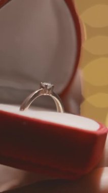 Çarpıcı bir nişan yüzüğünün yakın çekimi kırmızı kadife bir kutuda, aşk ve romantizmi somutlaştırıyor, sıcak bokeh ışıklarıyla güçlendirilmiş, Sevgililer Günü 'nü özel biriyle kutlamak için mükemmel.