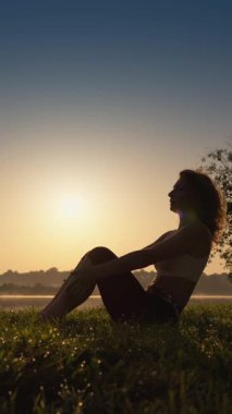 Gün batımında meditasyon yapan, yoga ve gevşemeyi somutlaştıran huzurlu bir kadın silueti, huzur dolu doğal bir ortamda vücut ve zihni uyumlu hale getiren, doğa güzelliğine ve sakinleştirici seslere dalmış bir kadın.