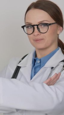 Şık gözlüklü ve beyaz önlüklü kendine güvenen bir kadın doktor, boynunda steteskopla tarafsız bir zemin üzerinde duruyor. Sağlık hizmetlerinde profesyonellik ve şefkat simgeliyor.