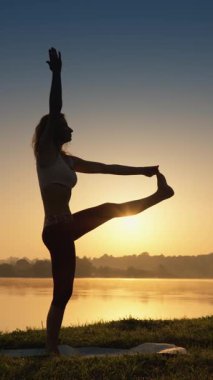 Güneş kıyı şeridinde batarken, bir kadın yoga yapıyor, vücudunu ve zihnini bu huzurlu anda derin bir huzur ve rahatlık için harmanlarken huzur ve dengeyi kucaklıyor.