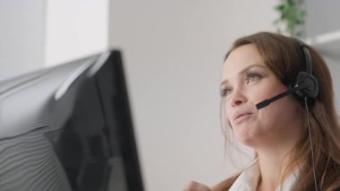 Modern bir ofiste, bir müşteri hizmetleri temsilcisi, kulaklıkla, özel destek sağlamak ve müşterilerin ihtiyaçlarını karşılamak için bilgisayar ekranını dikkatle gözlemleyerek bir sohbete girişir.