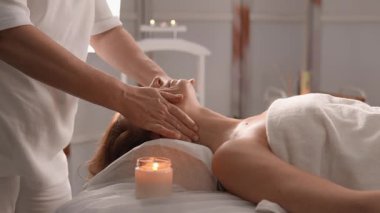 Sakin bir kaplıcada, yetenekli bir terapist sakin bir müşteriye rahatlatıcı bir yüz masajı yapar. Yumuşak, mum ışığında rahatlatıcı atmosfere iyi gelir.