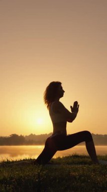 Gün batımında yoga yapan bir kadının güzel silueti yaklaşan yaz günlerine hazırlanmak için vücudunu ve zihnini ustalıkla birleştiren farkındalığın özünü gerçekten somutlaştırıyor.