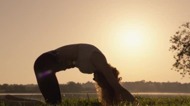 Gün batımında yoga yapan siluetli bir birey, iç uyumu ve huzuru simgeliyor, yumuşak güneş ışığı manzarayı ılık renklerde yıkıyor, sahneleri güzelleştiriyor ve huzur veriyor.