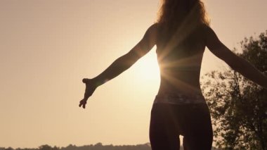 Parlak, renkli bir gün batımının nefes kesen arka planına karşı yoga yapan bir kadının huzurlu ve zarif silueti. Derin bir sükunet ve vücut ve ruhun mükemmel dengesi.