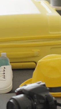 Parlak sarı bir bavul, içinde kamera, rahat spor ayakkabılar ve şık bir şapka gibi seyahat gereksinimleri barındırıyor. Maceralı bir yolculuk için hazırlanmanın heyecanını simgeliyor.